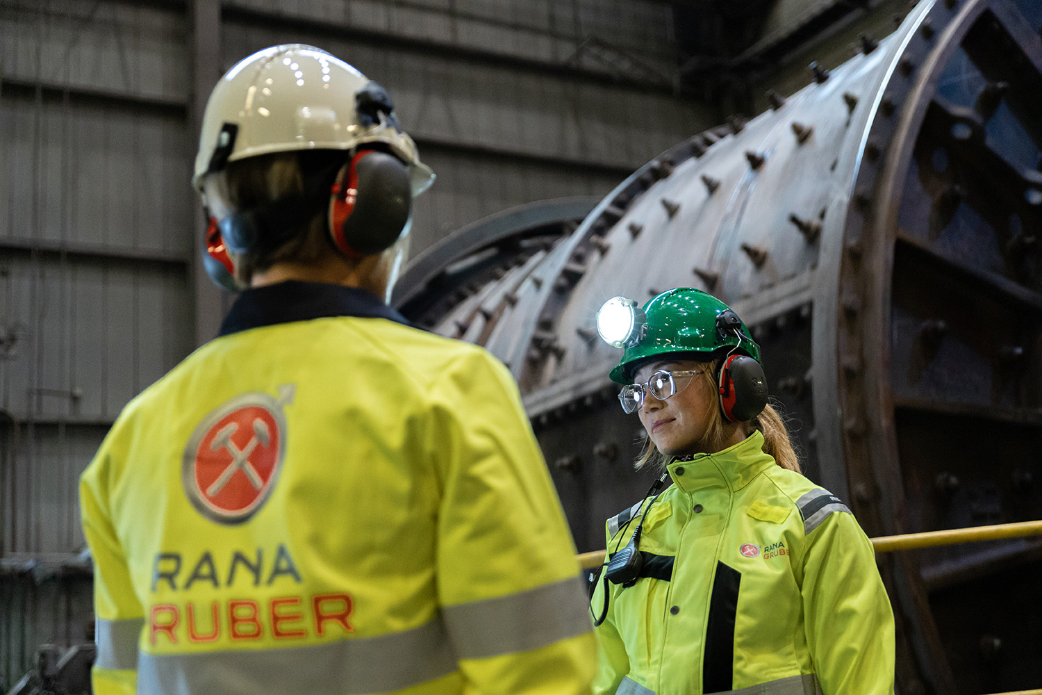 Två arbetare med varselkläder stående framför en autogen kvarn.