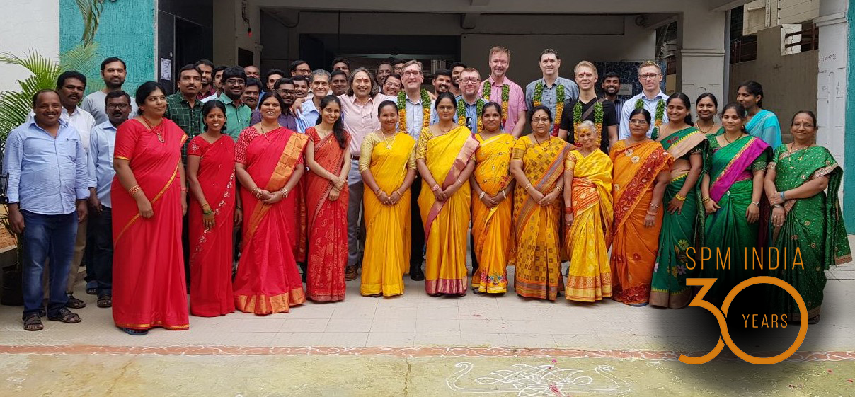 En grupp människor samlade framför en byggnad med kvinnor i färggranna indiska klänningar på främsta raden